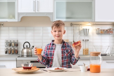 Photo of Cute little boy eating tasty toasted bread with jam at table in kitchen