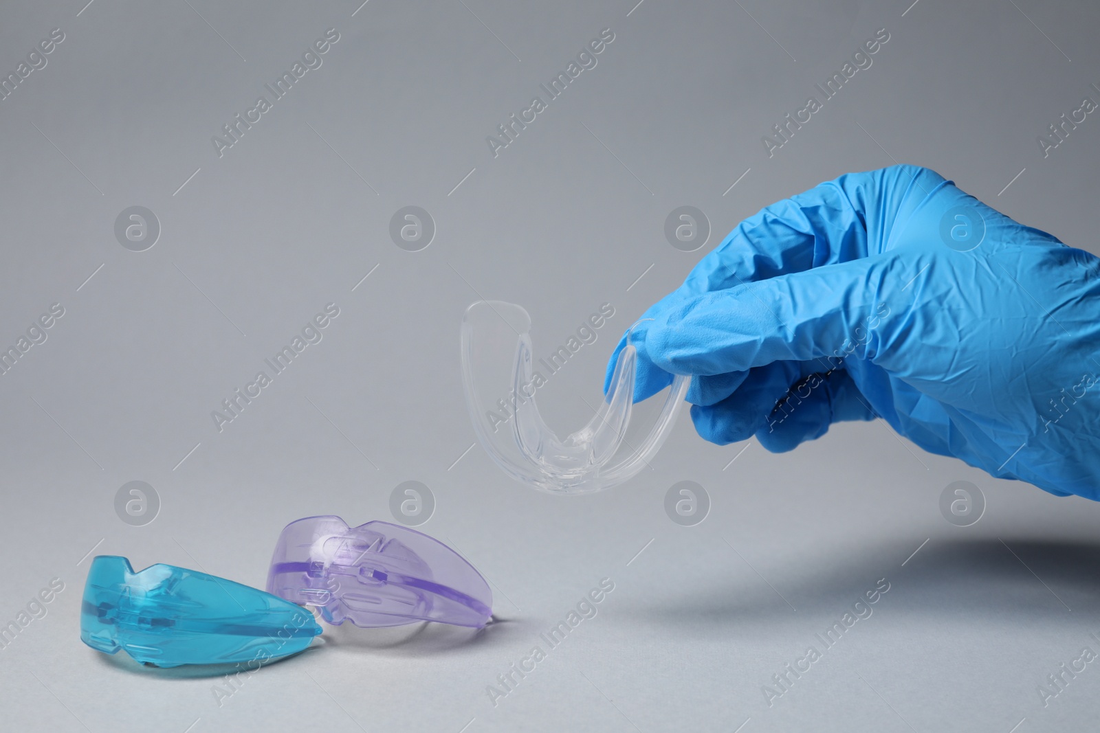 Photo of Dentist holding mouth guard on light grey background, closeup. Bite correction