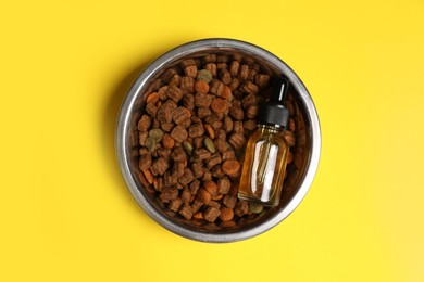 Glass bottle of tincture and dry pet food in bowl on yellow background, top view