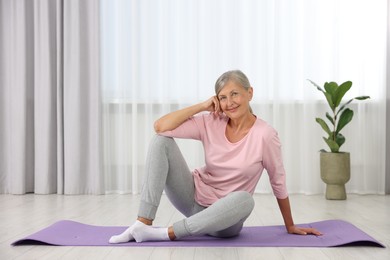 Happy senior woman sitting on mat at home. Yoga practice