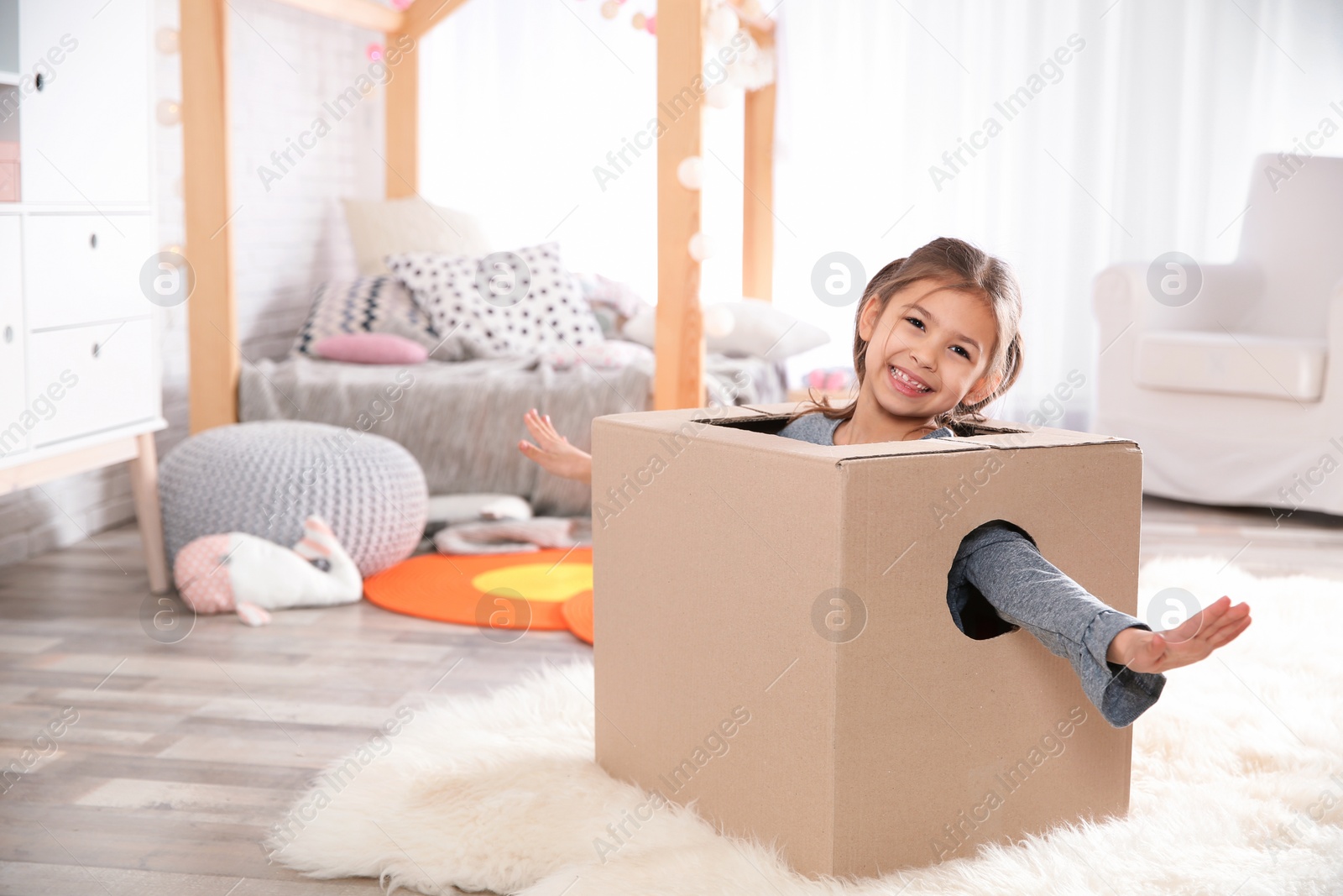 Photo of Cute little girl playing with cardboard box in bedroom