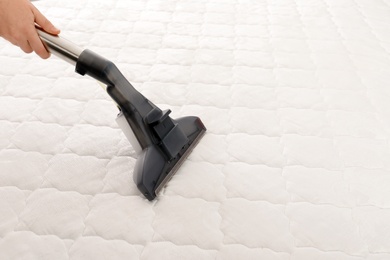 Woman disinfecting mattress with vacuum cleaner, closeup. Space for text