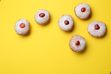 Photo of Hanukkah donuts with jelly and powdered sugar on yellow background, flat lay. Space for text
