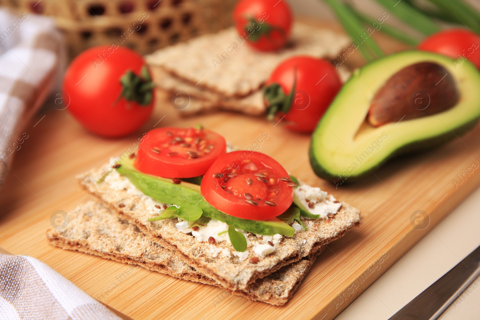 Photo of Tasty crispbreads with cream cheese, fresh tomatoes and avocado on beige table, closeup. Space for text