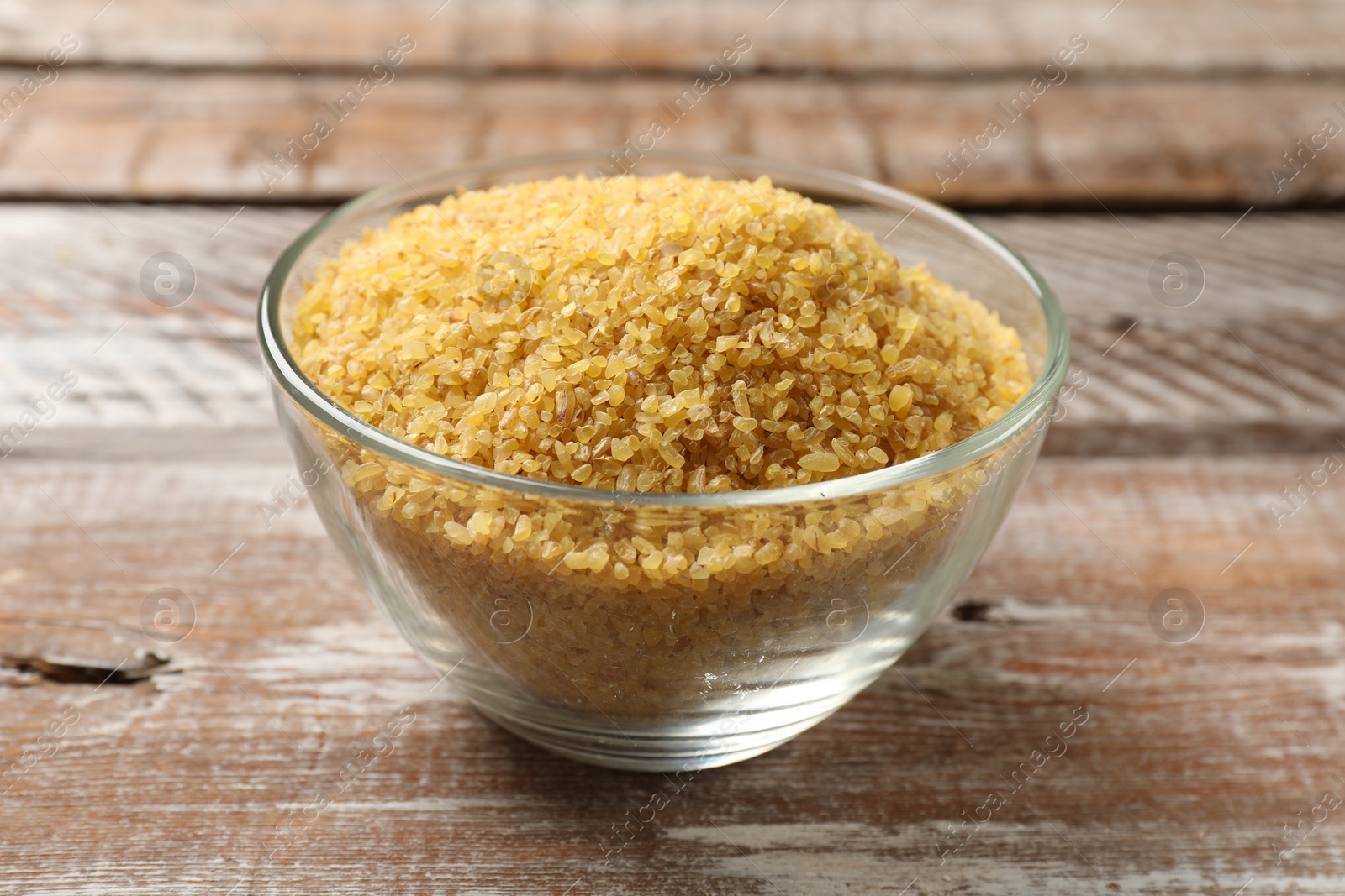 Photo of Raw bulgur in bowl on wooden table, closeup