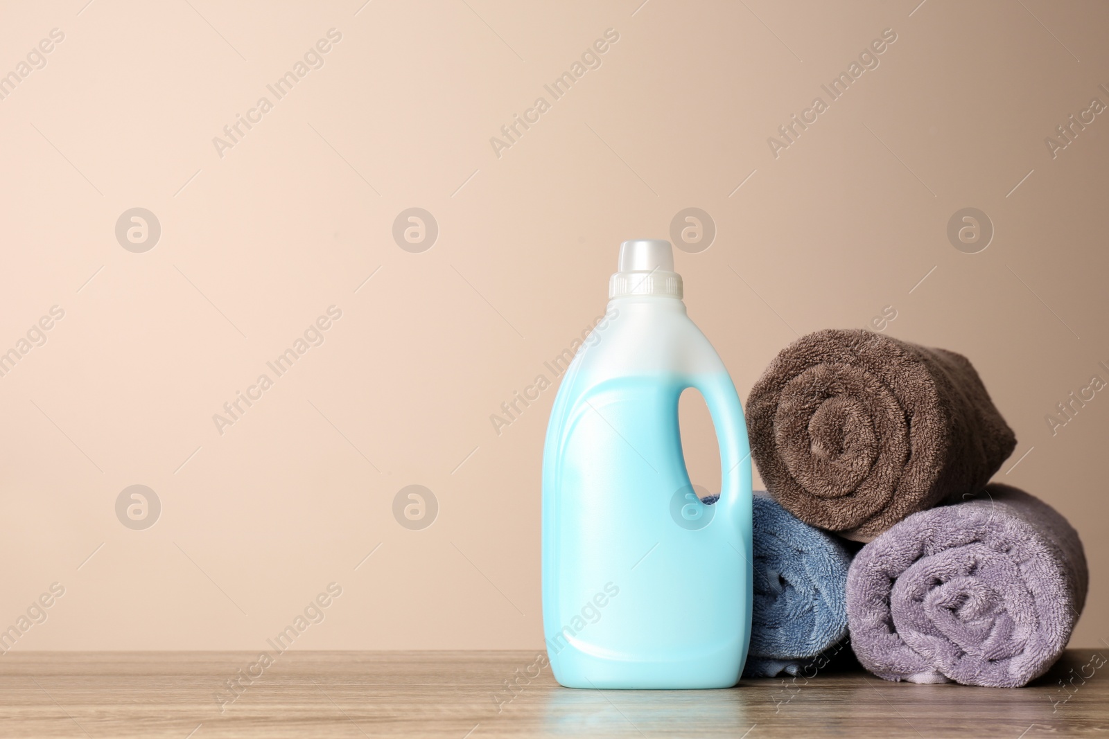 Photo of Bottle of detergent and clean towels on table against color background, space for text. Laundry day