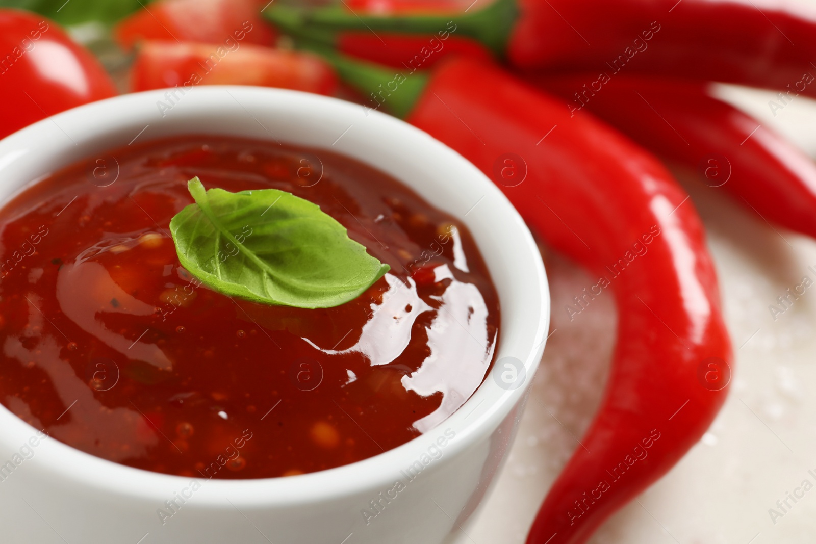 Photo of Spicy chili sauce with basil on light table, closeup