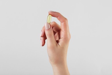 Woman holding vitamin capsule on grey background, closeup. Health supplement