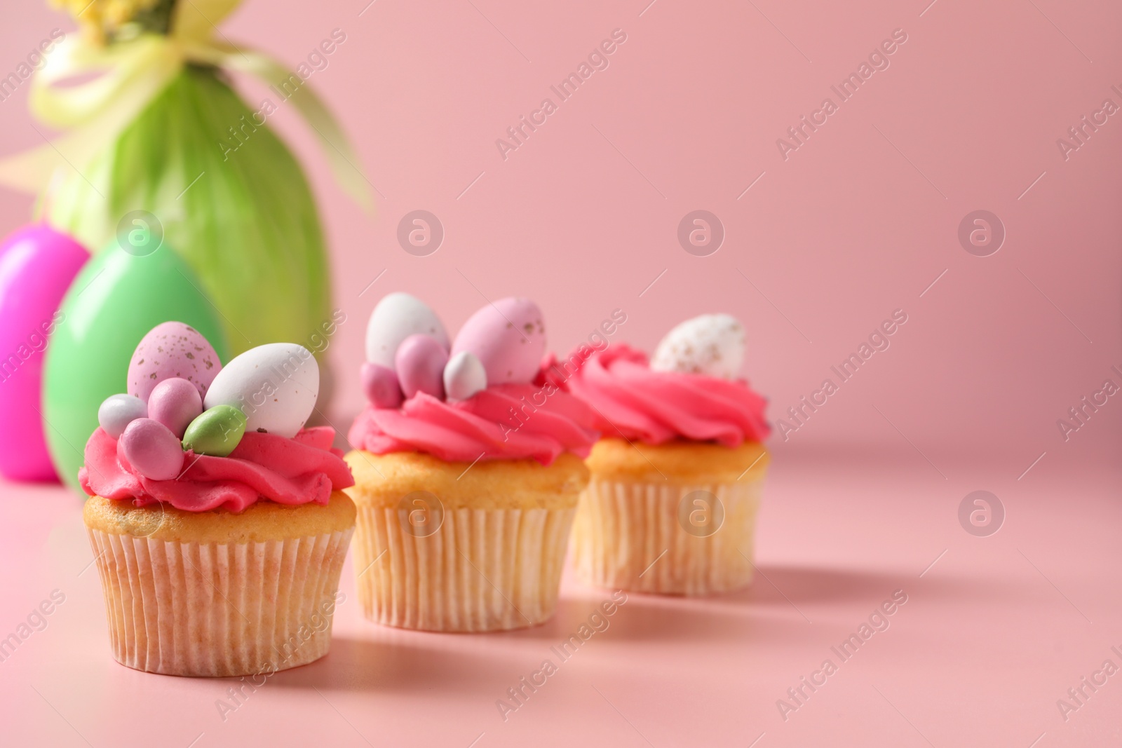 Photo of Tasty decorated Easter cupcakes on pink background, selective focus. Space for text