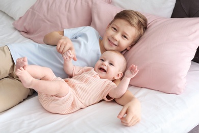 Cute little baby with elder brother lying on bed at home