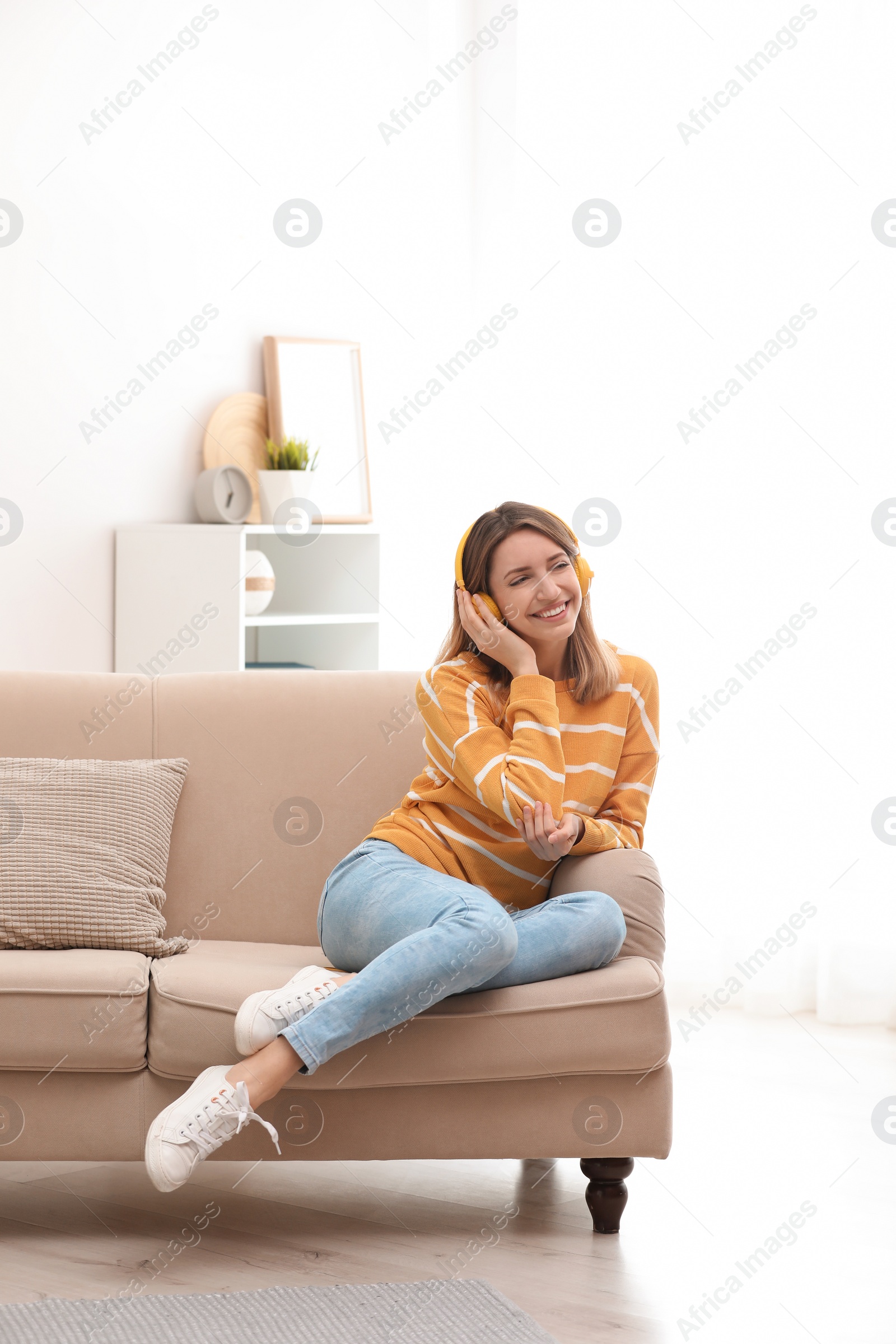 Photo of Young woman in headphones enjoying music on sofa at home