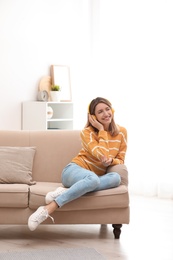 Young woman in headphones enjoying music on sofa at home