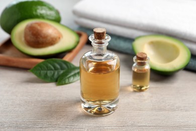 Bottles of essential oil, fresh avocado and towels on light wooden table