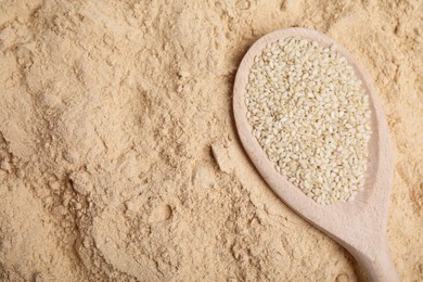 Photo of Spoon with sesame seeds on flour, top view. Space for text