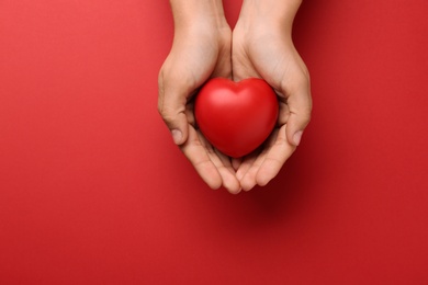 Photo of Woman holding decorative heart on red background, top view