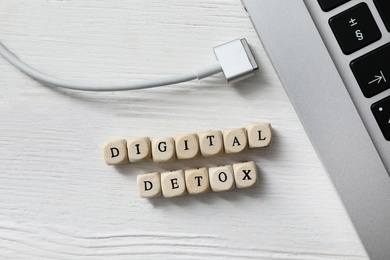 Photo of Cubes with words DIGITAL DETOX and disconnected charging cable on white wooden background, flat lay