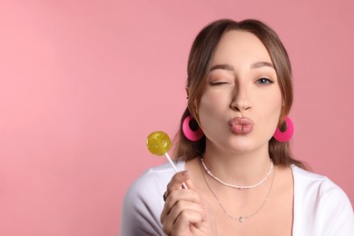 Photo of Young woman with lip and ear piercings holding lollipop on pink background, space for text