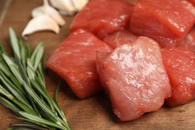 Photo of Cooking delicious goulash. Raw beef meat and rosemary on wooden table, closeup