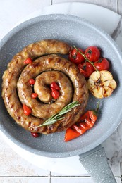 Delicious homemade sausage with garlic, tomatoes, rosemary and chili in frying pan on light tiled table, top view
