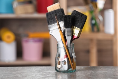 Photo of Glass jar with paint brushes on table in workshop. Space for text
