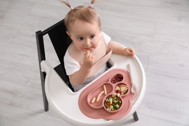 Photo of Cute little baby eating food in high chair indoors, above view