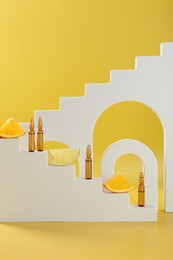 Stylish presentation of skincare ampoules with vitamin C and citrus slices on yellow background