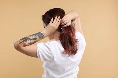 Stylish tattooed woman on beige background, back view
