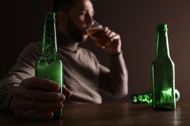 Photo of Addicted man drinking alcohol at wooden table indoors, focus on hand