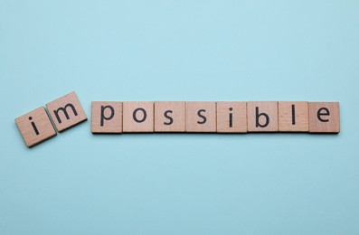Photo of Motivation concept. Changing word from Impossible into Possible by removing wooden squares on light blue background, flat lay