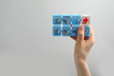 Photo of Woman holding plastic box with different pills on light grey background, closeup. Space for text