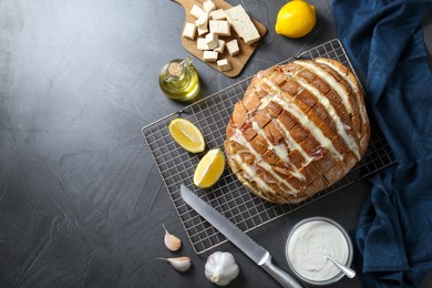 Photo of Freshly baked bread with tofu cheese, ingredients and knife on black table, flat lay. Space for text