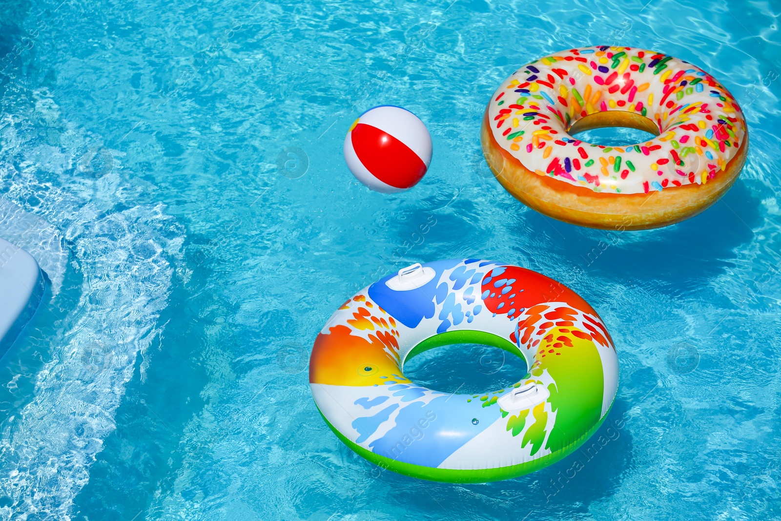 Photo of Bright inflatable rings and beach ball floating in swimming pool on sunny day. Space for text