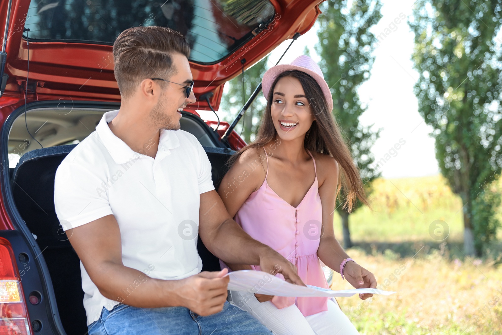 Photo of Young couple with map sitting in open car trunk outdoors