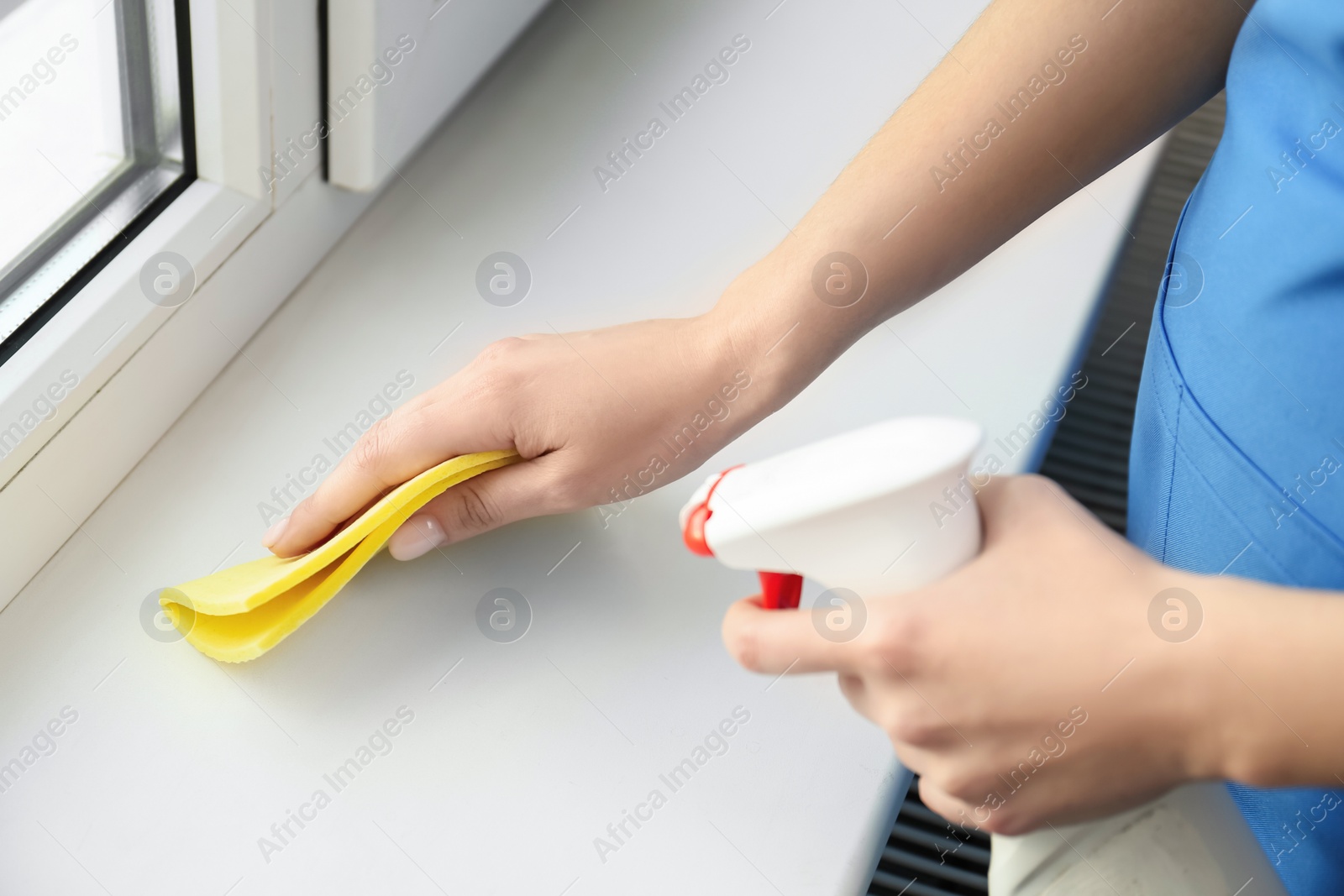 Photo of Woman cleaning window sill with rag and detergent indoors, closeup