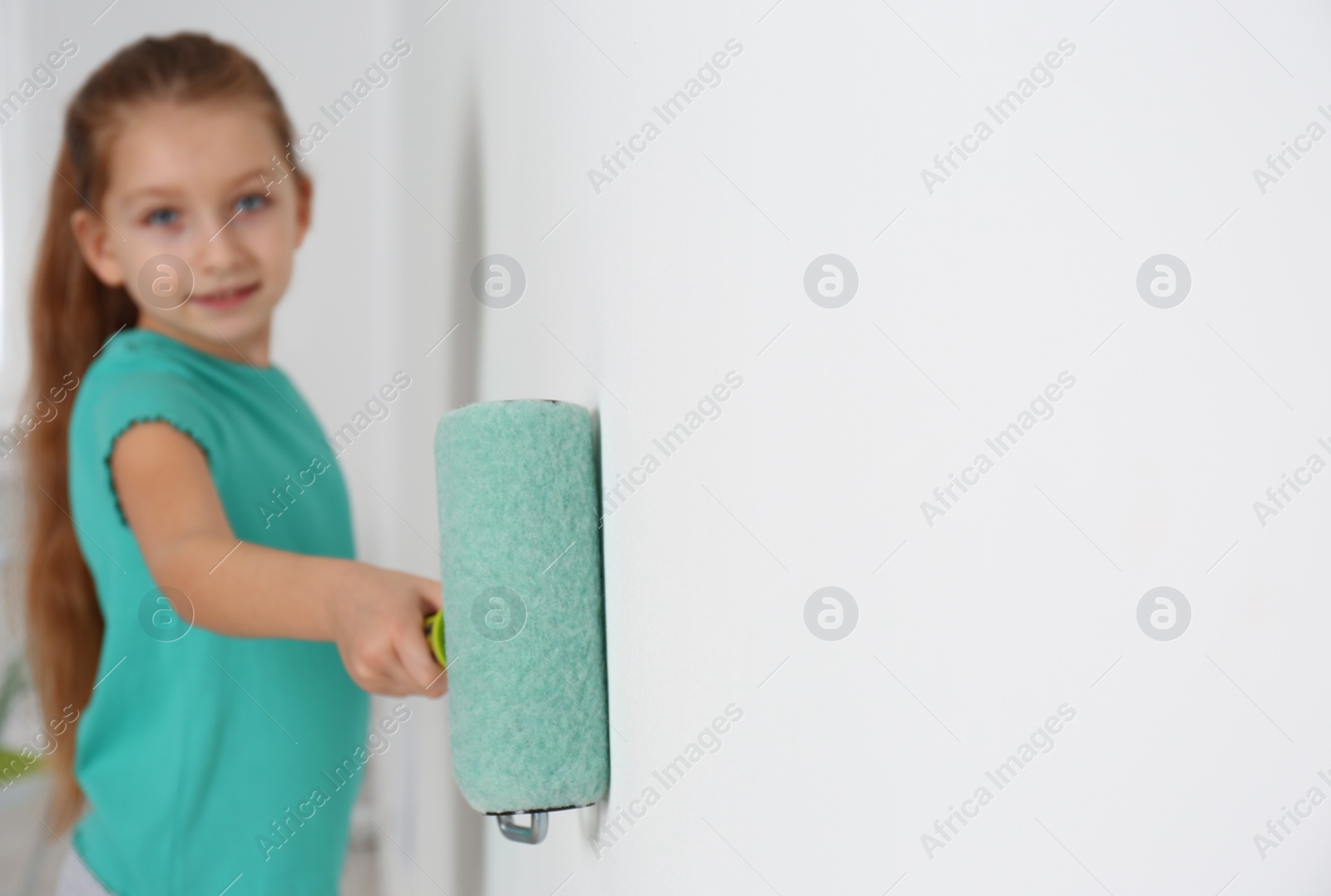 Photo of Little child painting with roller brush on white wall indoors. Space for text