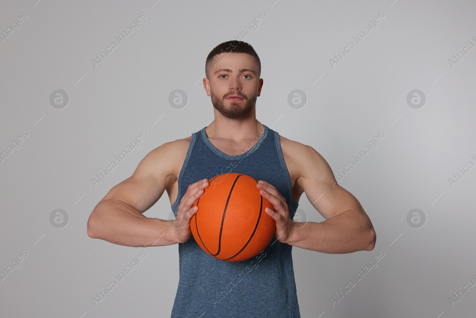 Photo of Athletic young man with basketball ball on light grey background