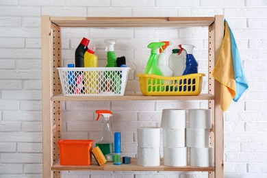 Photo of Shelving unit with detergents and toilet paper near white brick wall