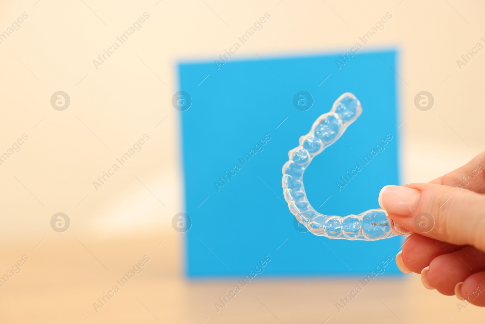 Photo of Woman with transparent dental aligner on blurred background, closeup. Space for text