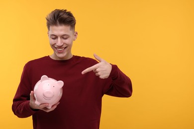 Photo of Happy man pointing at piggy bank on yellow background. Space for text