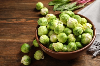 Photo of Bowl of fresh Brussels sprouts on wooden table. Space for text