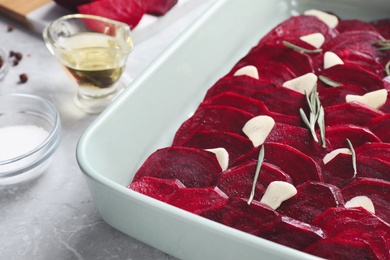 Baking dish with raw beetroot slices, garlic and rosemary on light marble table, closeup