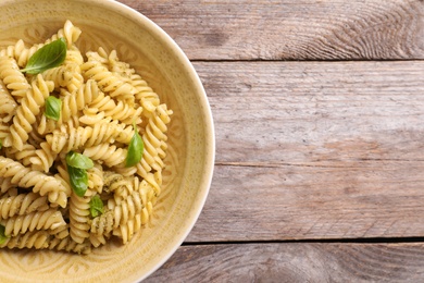 Photo of Plate of delicious basil pesto pasta on wooden background, top view with space for text