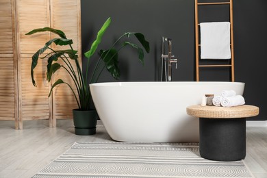 Spa day. Ceramic tub, houseplant and wicker table in bathroom