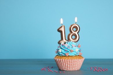 Photo of Coming of age party - 18th birthday. Delicious cupcake with number shaped candles on light blue background, space for text