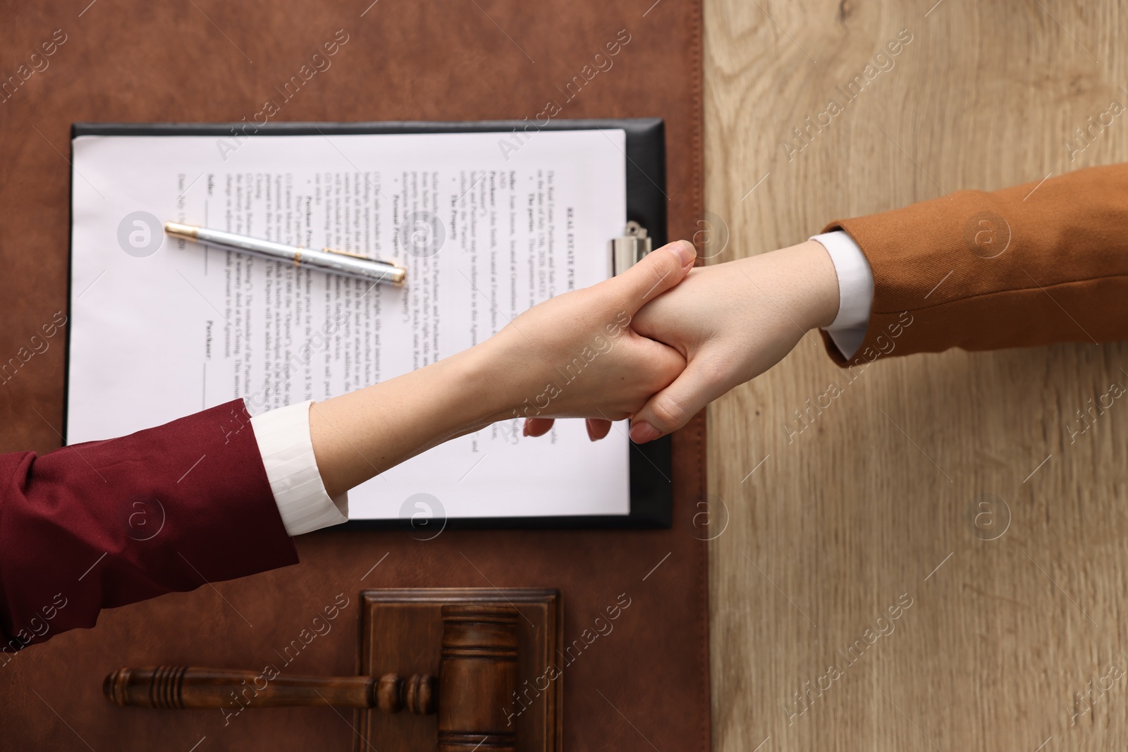 Photo of Notary shaking hands with client at wooden table, top view