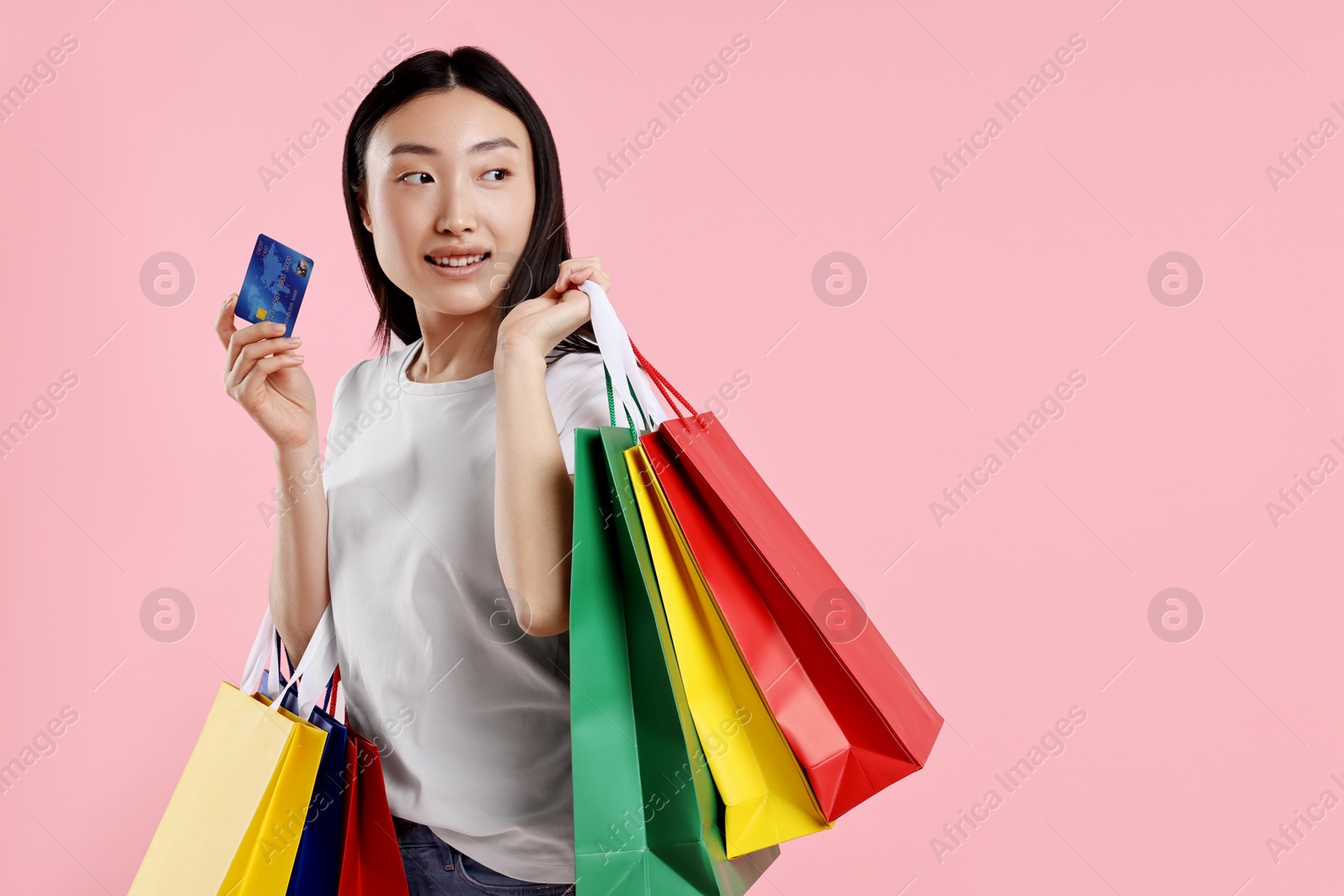 Photo of Smiling woman with shopping bags and credit card on pink background. Space for text