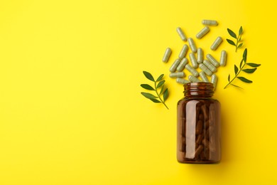 Photo of Vitamin pills, branches and bottle on yellow background, flat lay. Space for text