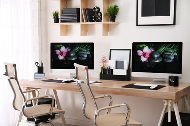 Photo of Modern workplace with large desk and computers in room. Stylish interior