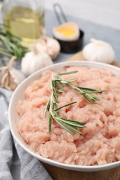 Fresh raw minced meat and rosemary in bowl on table, closeup