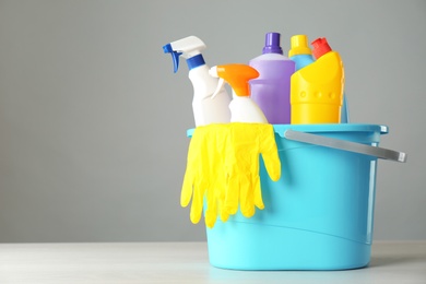 Photo of Bucket with cleaning products and gloves on grey table. Space for text